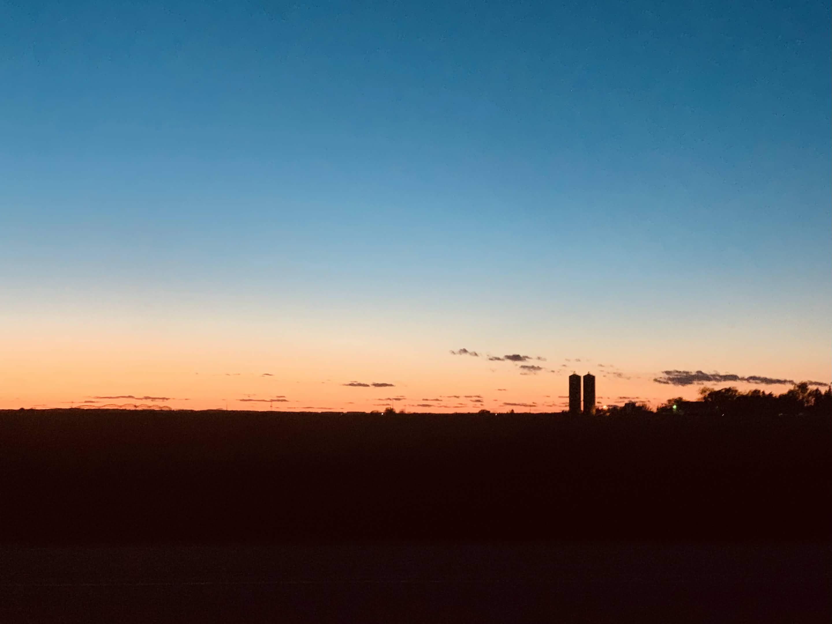 A field and grain silos at sunset.